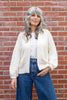 Model wearing Boucle Jonah Sweater in Natural, Minnie Tank in White, and blue jeans, standing in front of brick wall