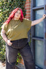 Model wearing Jones Top in Fennel and black jeans in front of vine-covered brick wall next to glass windows