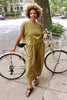 Model wearing Jones Top and Larkin pants both in Fennel, leaning against white bicycle on neighborhood sidewalk