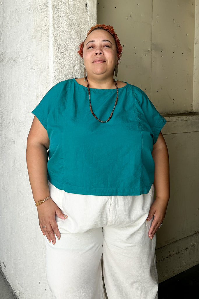 Model wearing Jones Top in Ocean and Cadence Pants in White, standing in front of a white building