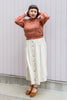 Model wearing Roni Sweater in Rust Melange and white button up skirt standing in front of white wall