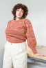 Model wearing Joni Sweater in Rust Melange and Painter Pants in Natural, leaning on table in front of white background