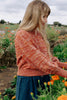 Model wearing Roni Sweater in Rust Melange, walking through field of orange flowers