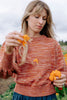 Model wearing Roni Sweater in Rust Melange holding orange flowers and scattering petals