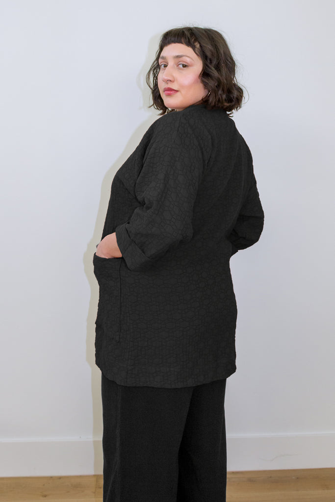 Back/side view of model wearing Jules Cardigan in Black and Atlas Pant in Black, in front of white wall
