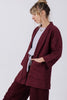 Side view of model wearing Jules Cardigan in Burgundy, Ayana Top in Mist, and Atlas Pant and Burgundy, standing with one hand in a pocket, in front of white background