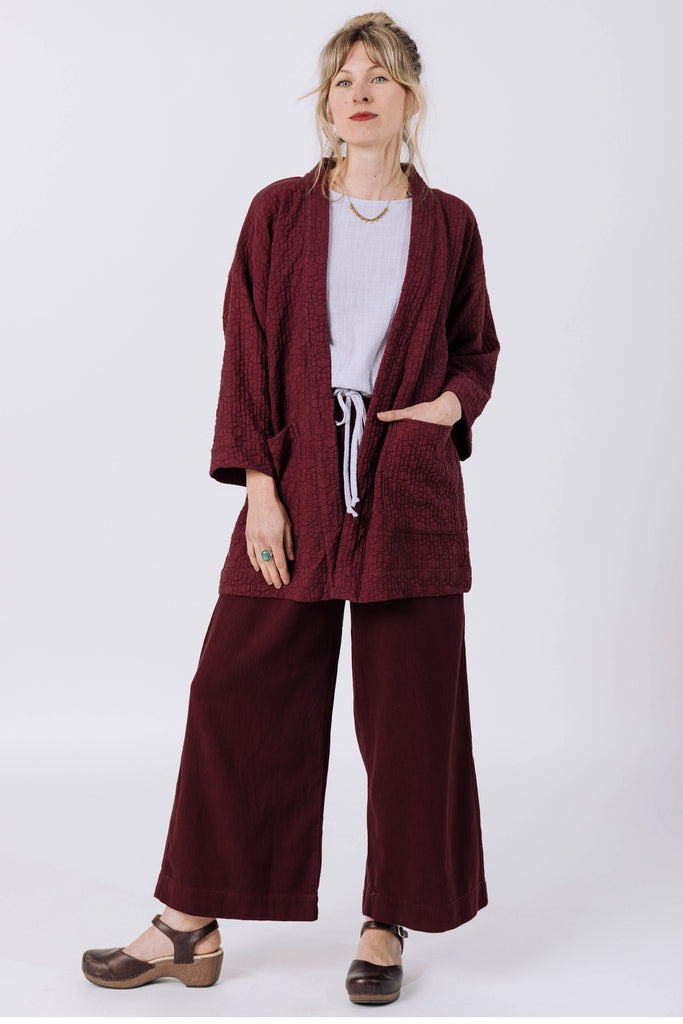 Model wears Jules Cardigan in Burgundy, Ayana Top in Mist, and Atlas Pant and Burgundy, standing with one hand in a pocket, in front of white background