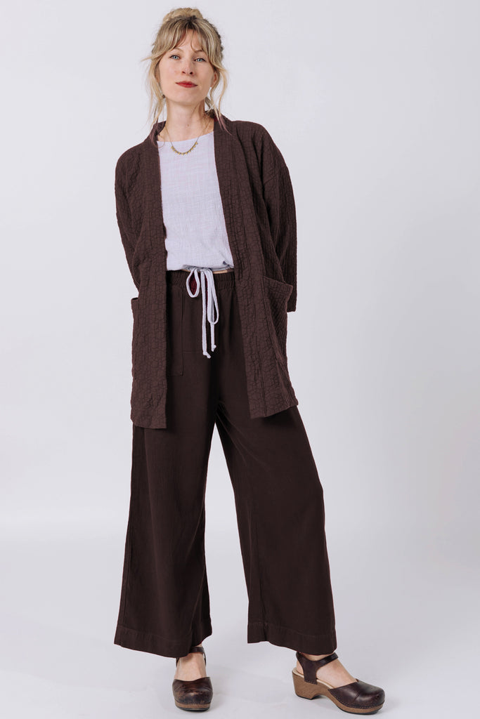 Front view of model wearing Jules Cardigan in Chocolate, Ayana Top in Mist, and Atlas Pant in Chocolate, standing  in front of white wall
