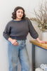 Model wearing Lana Sweater in Charcoal and light wash jeans, leaning on table in front of white background