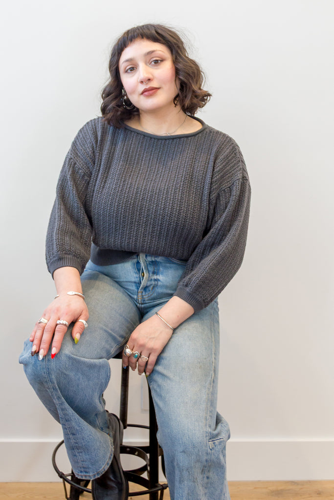 Model wearing Lana Sweater in Charcoal and light wash jeans, sitting on a stool in front of white background