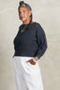 Lana Sweater in Charcoal and Cadence Pant in White on model standing with hands in pockets, in front of white background