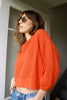 Model wearing Lana Sweater in Tomato and light wash jeans, standing in open doorway with stairs leading into the building