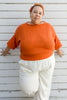 Model wearing Lana Sweater in Tomato and Cadence Pants in White, leaning against white wall