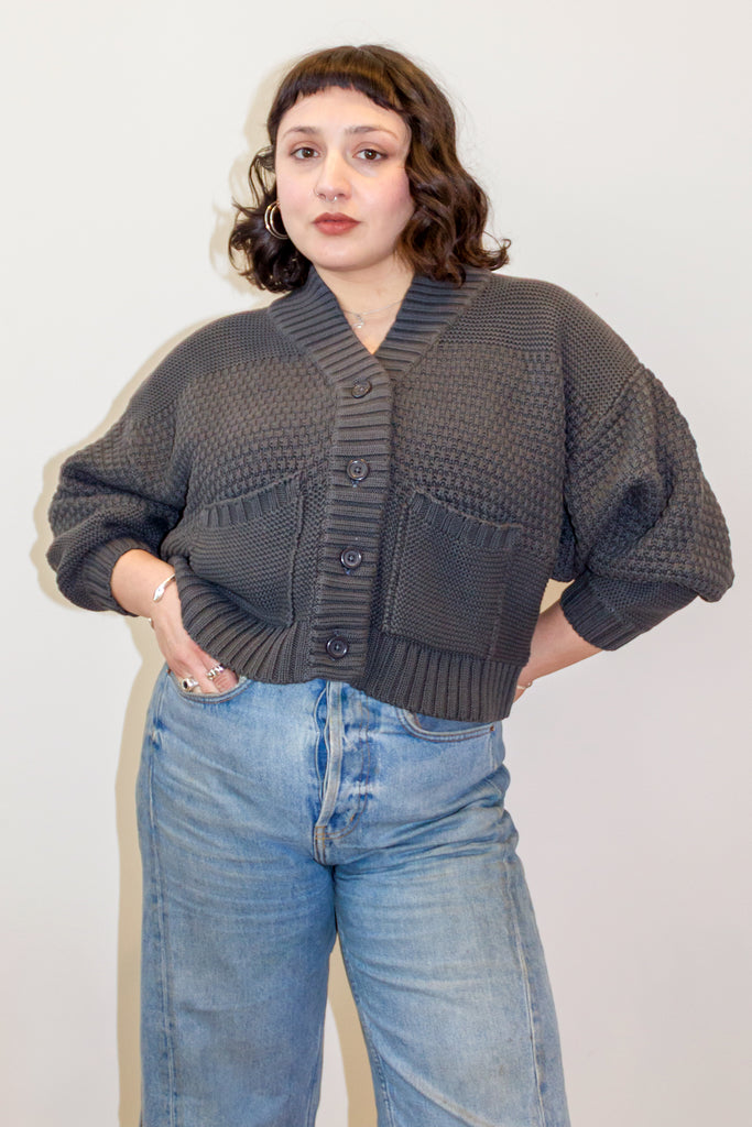 Person wearing a dark gray knitted Lino cardigan and blue jeans against a white background