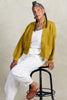 Model wearing Lino Cardigan in Chartreuse and Cadence Pant in White sitting on wood and black metal stool in front of white background