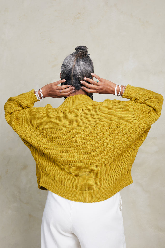 Back view of model wearing Lino Cardigan in Chartreuse and Cadence Pant in White in front of white background