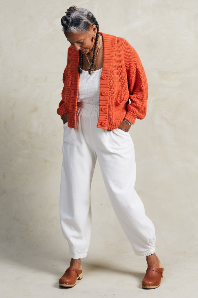 Lino Cardigan in Tomato and Cadence Pant in White on model with hands in pockets, in front of white background