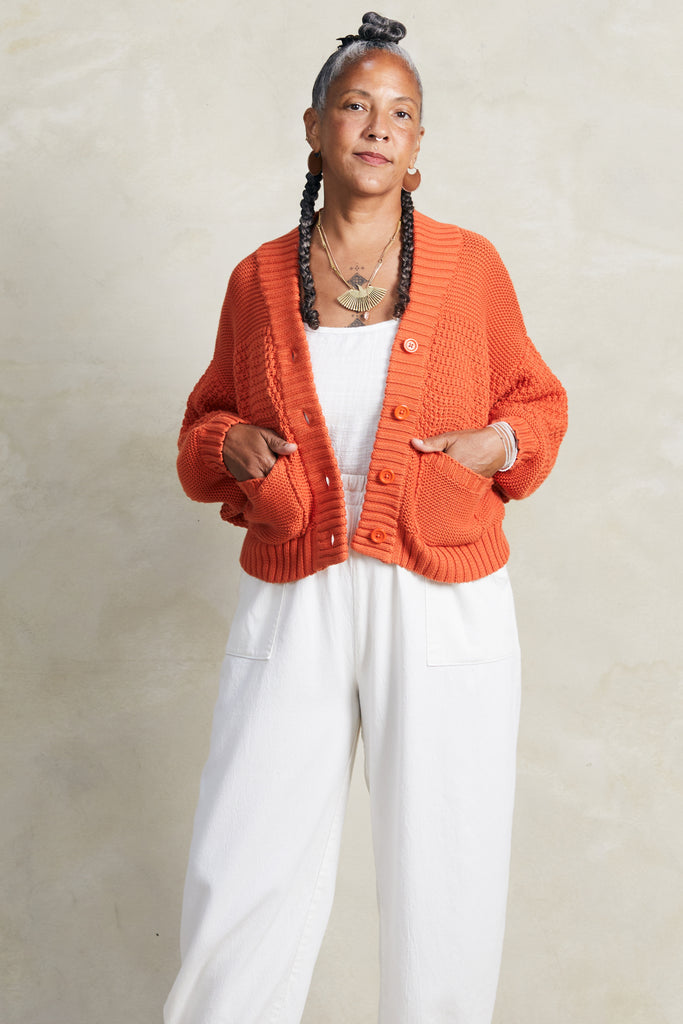 Lino Cardigan in Tomato and Cadence Pant in White on model with hands in pockets, in front of white background