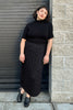 Model wearing Short Sleeve Rib Turtleneck in Black and Mae Sweater Skirt in Black leaning in stone doorway