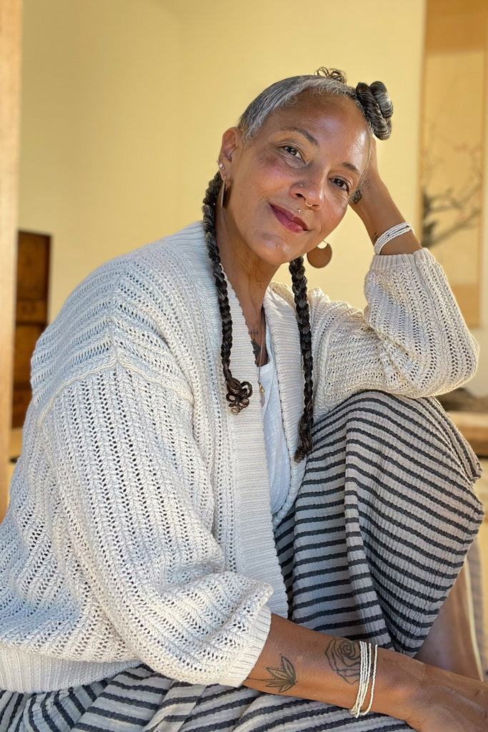Side view of Maeva Cardigan in Biscuit paired with Fawn Skirt in Oat on sitting model in front of yellow background