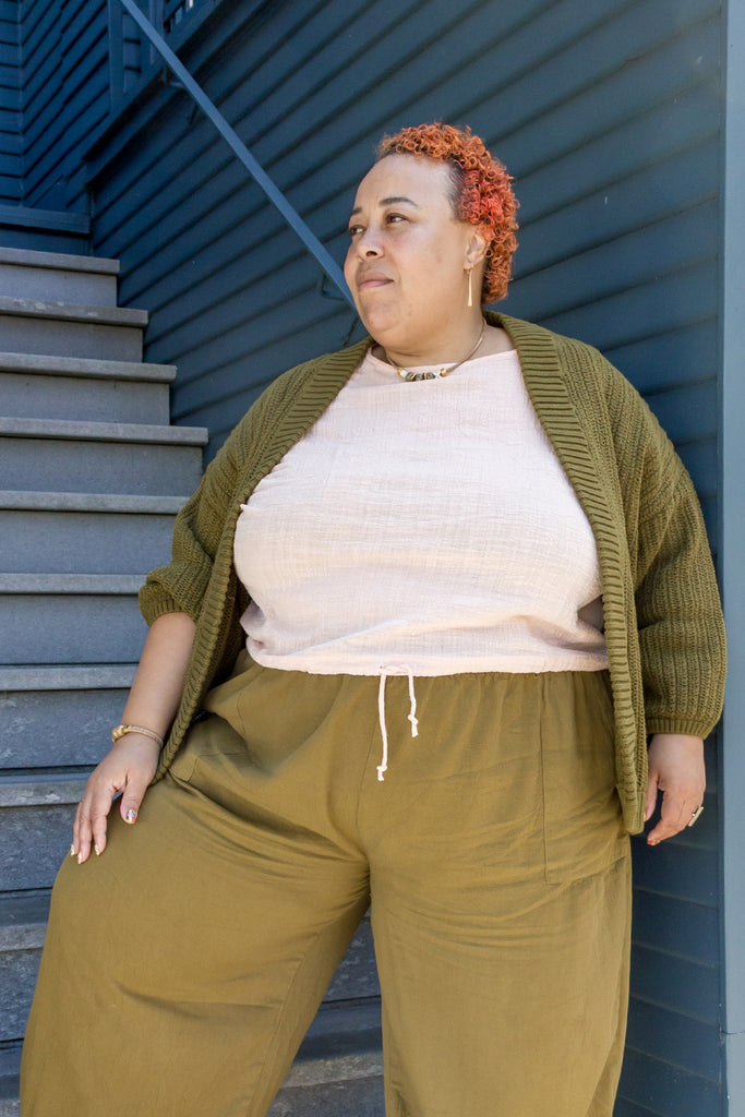Model wearing Maeva Cardigan in Fennel, Ayana Top in Peach, and Larkin Pants in Fennel, in front of blue building with white stairs