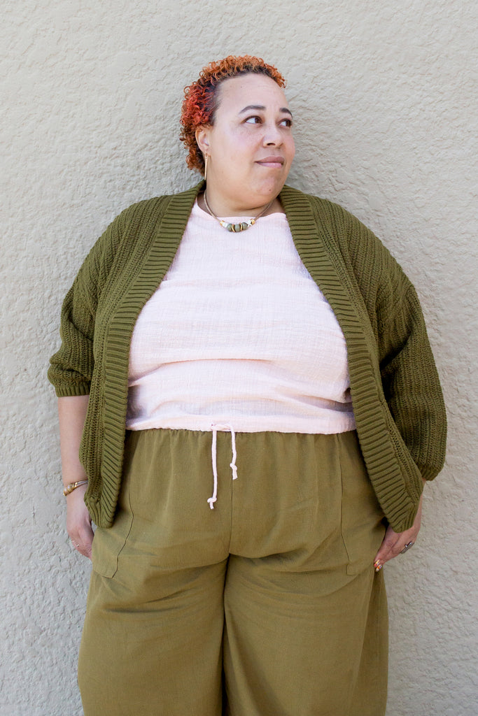 Model wearing Maeva Cardigan in Fennel, Ayana Top in Peach, and Larkin Pants in Fennel, leaning against white wall