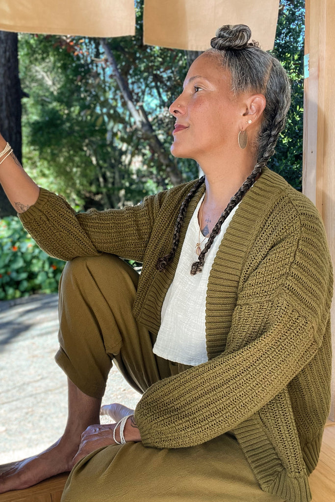 Maeva Cardigan in Fennel and Cadence Pants in Fennel on model sitting in doorway with trees in the background