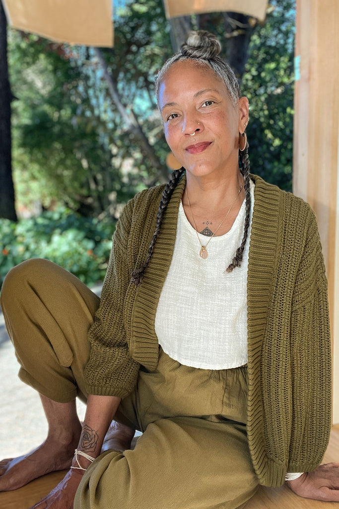 Maeva Cardigan in Fennel, Minnie Tank in White, and Cadence Pants in Fennel on model sitting in doorway with trees in the background