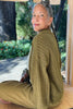 Side view of sitting model wearing Maeva Cardigan in Fennel and Cadence Pants in Fennel with nature in the background