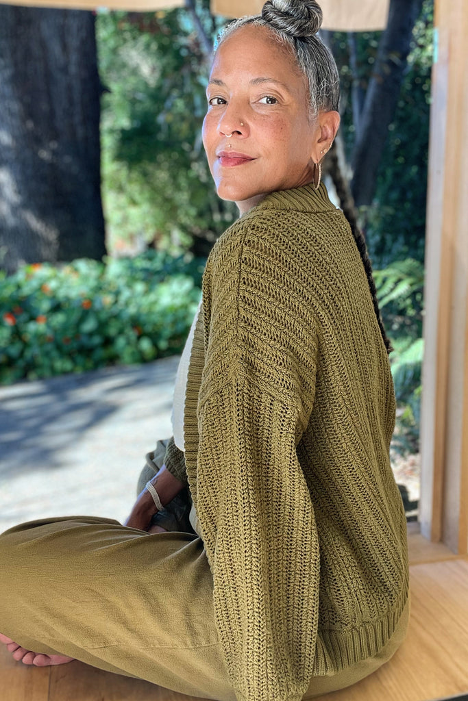 Side view of sitting model wearing Maeva Cardigan in Fennel and Cadence Pants in Fennel with nature in the background
