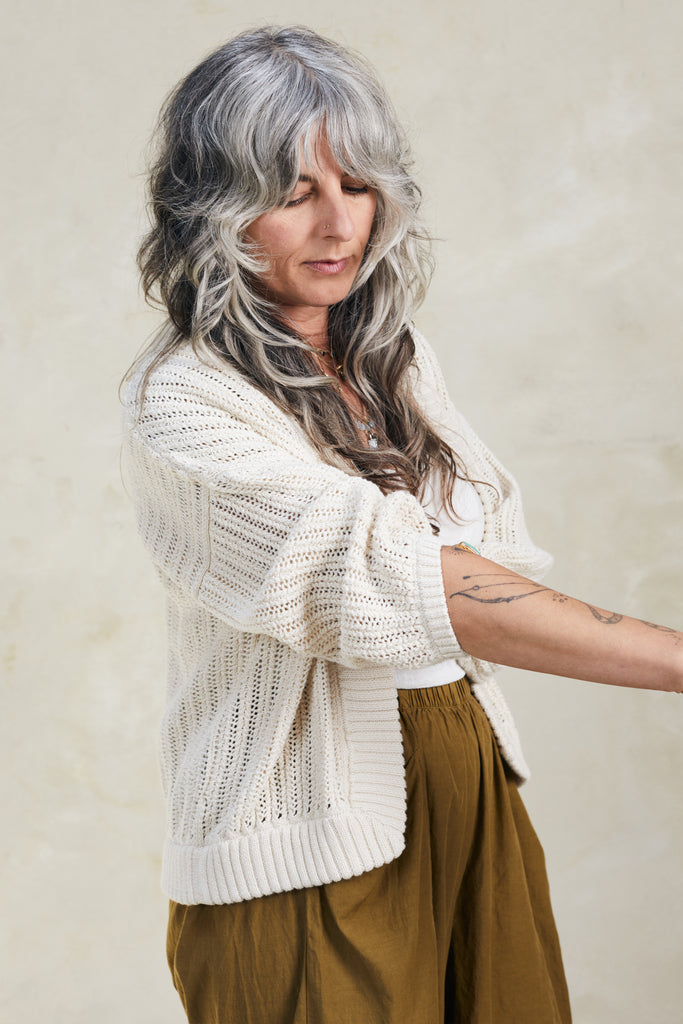 Model wearing Maeva Cardigan in Biscuit and rolling sleeve up in front of white background