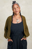 Model wearing Maeva Cardigan in Fennel with black top and pant, standing with hands in pockets in front of white background