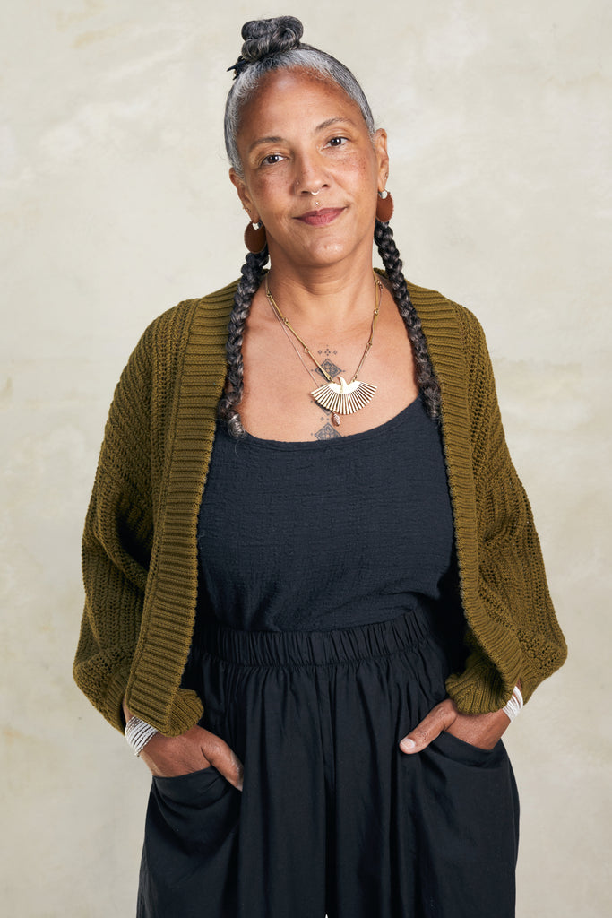 Model wearing Maeva Cardigan in Fennel with black top and pant, standing with hands in pockets in front of white background