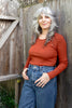 Model wearing Maisie Long Sleeve in Brick and jeans in front of wooden wall