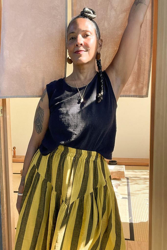 Front view of Minnie Tank in Black paired with Jessie Stripe Skirt in Dijon on model leaning against doorway