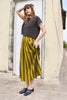 Model wearing Niko Sweater in Charcoal and Jessie Stripe Skirt in Dijon in front of white door of light yellow building