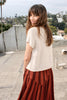 Model wearing Niko Top in Cream and Jessie Skirt in Brick/Black Stripe, on rooftop overlooking trees and neighboring buildings
