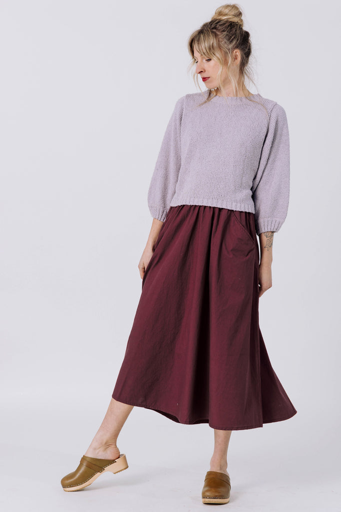Model wearing Nova Sweater in Mist and Fawn Skirt in Burgundy in front of white background