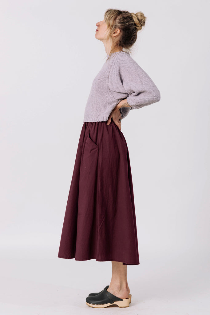 Side view of model wearing Nova Sweater in Mist and Fawn Skirt in Burgundy in front of white background