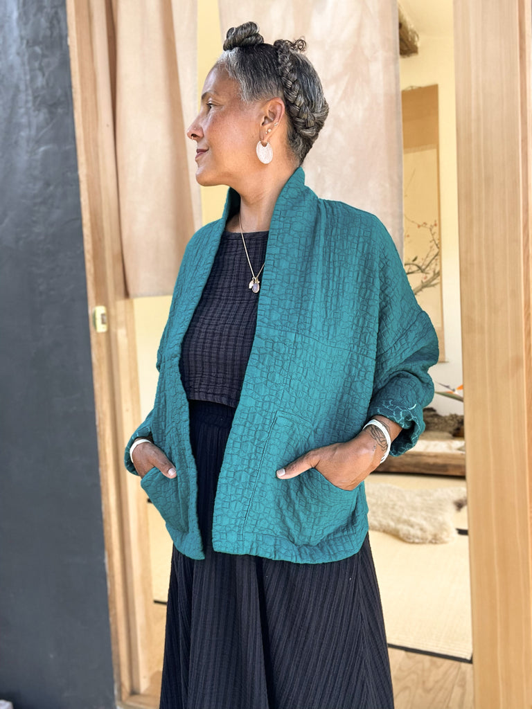 Oona Cardigan in Ocean on model, with hands in pockets, in front of wooden doorway.