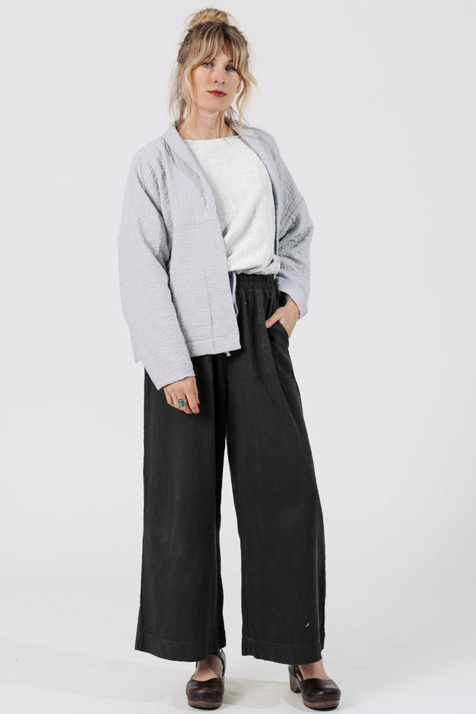 Front view of Atlas Pant in Black on model, paired with Oona Cardigan in Oyster, in front of white wall