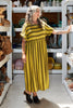 Front view of Perry Stripe Dress in Dijon on model standing in room with shelves of ceramics