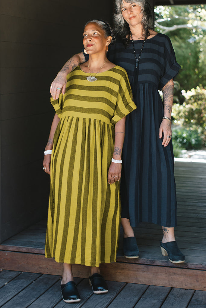 Two models wearing Perry Stripe Dresses. Model in foreground wears the dress in Dijon, and the model behind them (a step up) wears the dress in Black.