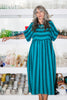 Woman wearing a Perry Dress in teal and black stripeds standing in a pottery studio.