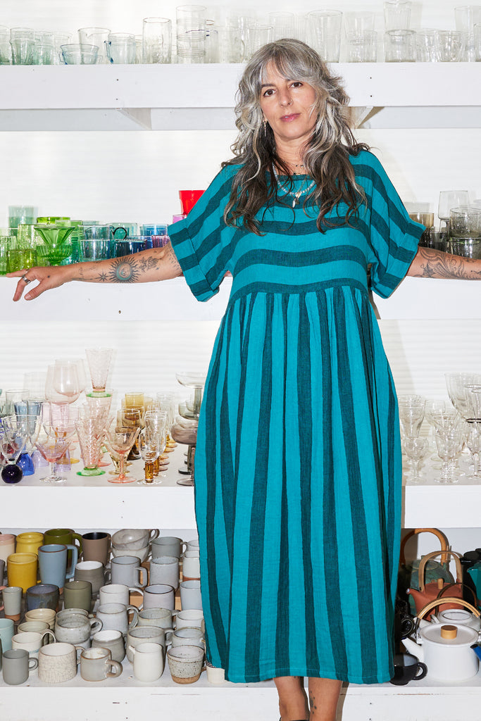 Woman wearing a Perry Dress in teal and black stripeds standing in a pottery studio.