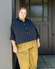 Model wearing Cropped Poet Blouse in Black and Cadence Pants in Dijon, standing in front of a grey door