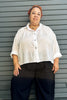 Model wearing Cropped Poet Blouse in White and Cadence Pant in Black, in front of dark green paneled wall