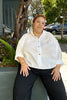 Model wearing Cropped Poet Blouse in White and Cadence Pant in Black, sitting on dark green ledge
