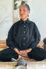 Model wearing a Cropped Poet Blouse in Black and Cadence Pants in Black, sitting with a teapot in front of them