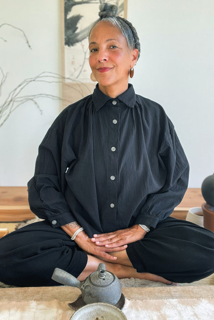 Model wearing a Cropped Poet Blouse in Black and Cadence Pants in Black, sitting with a teapot in front of them